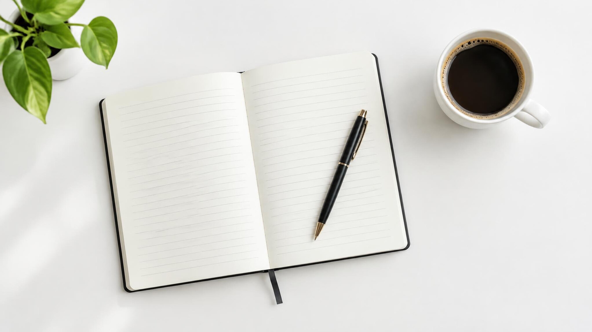 Open notebook with pen and a cup of coffee on a clean white desk